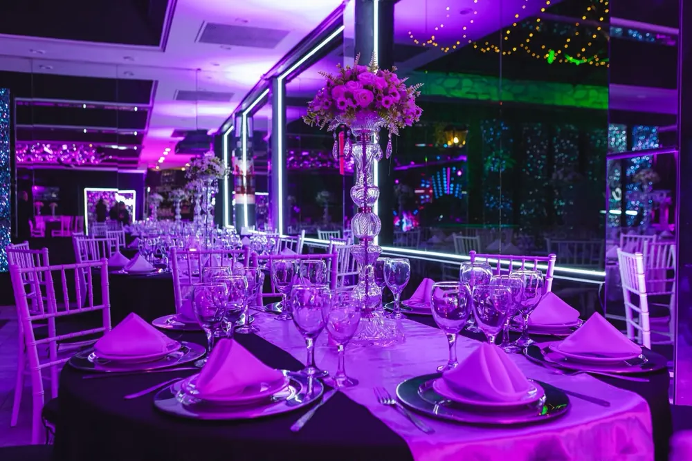 Mesa servida con copas y centro de flores bajo luz violeta en Eclipse Eventos
